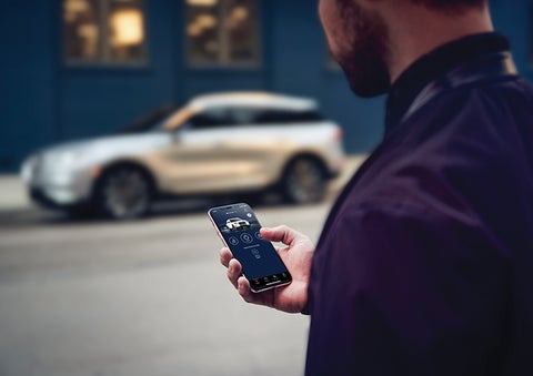 A person is shown interacting with a smartphone to connect to a Lincoln vehicle across the street. | Parks Lincoln of Gainesville in Gainesville FL