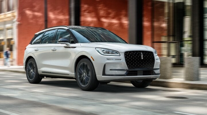 A white 2025 Lincoln Corsair® SUV with the Jet Appearance Package is being driven through a city.| Parks Lincoln of Gainesville in Gainesville FL