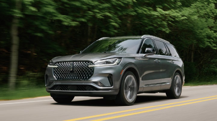 A 2027 Lincoln Aviator® SUV is being driven down a road lined with trees. | Parks Lincoln of Gainesville in Gainesville FL